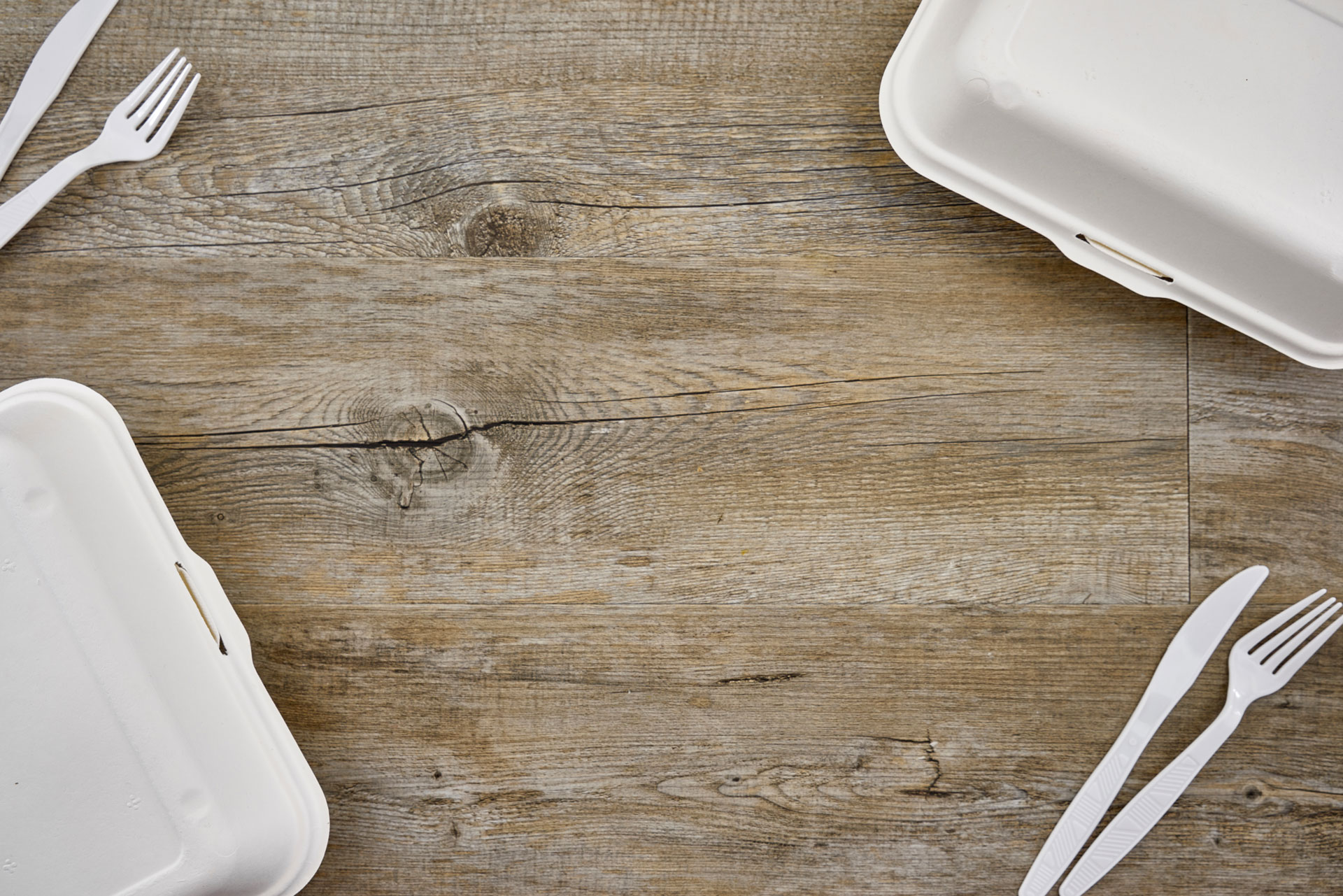 Biodegradable plastic containers and biodegradable plastic cutlery on a wooden surface.