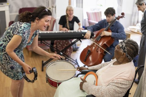 A group of people with dementia playing musical instruments, assisted by a Music in Mind therapist.