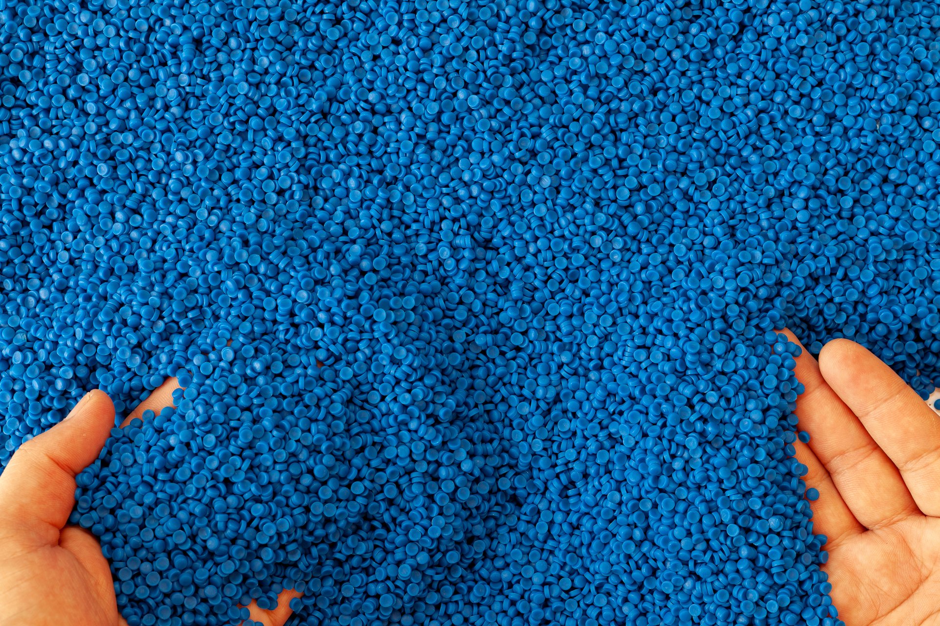 Close-up of plastic polymer granules with hands running through them.