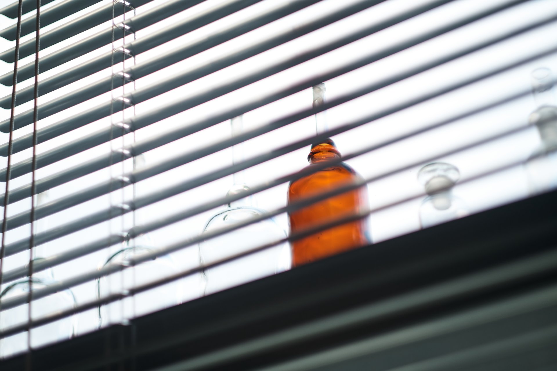 Bottles sit on windowsill behind blind - Innovation Factory