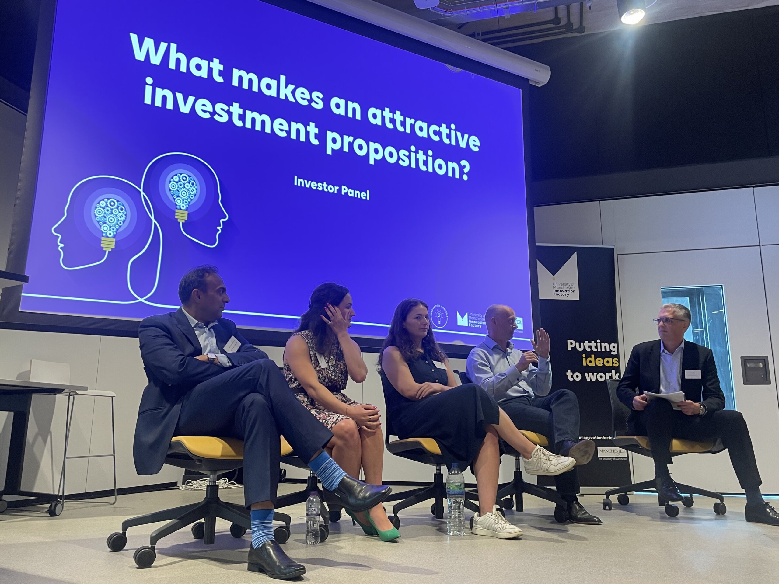 3 men and 2 women sit in discussion in front of a screen reading "What makes an attractive investment proposition?"