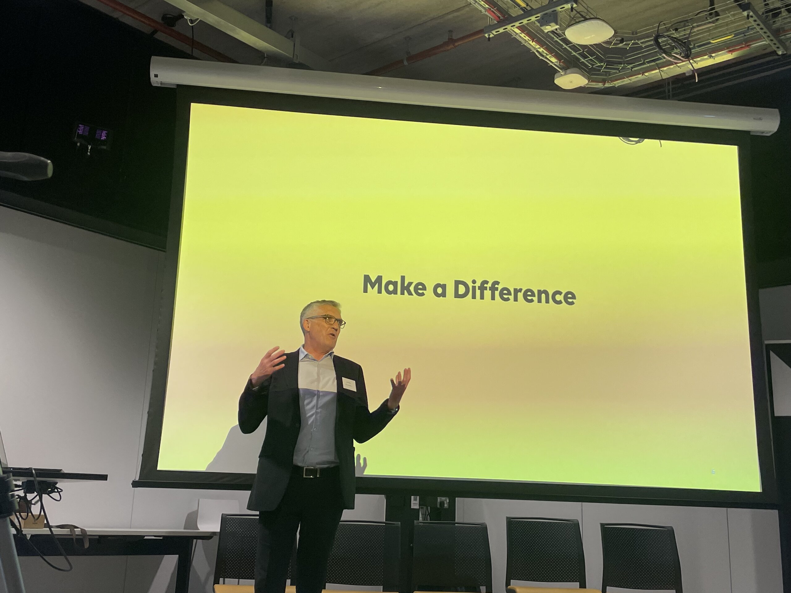 A man stands in front of a slide which reads "Make a Difference"