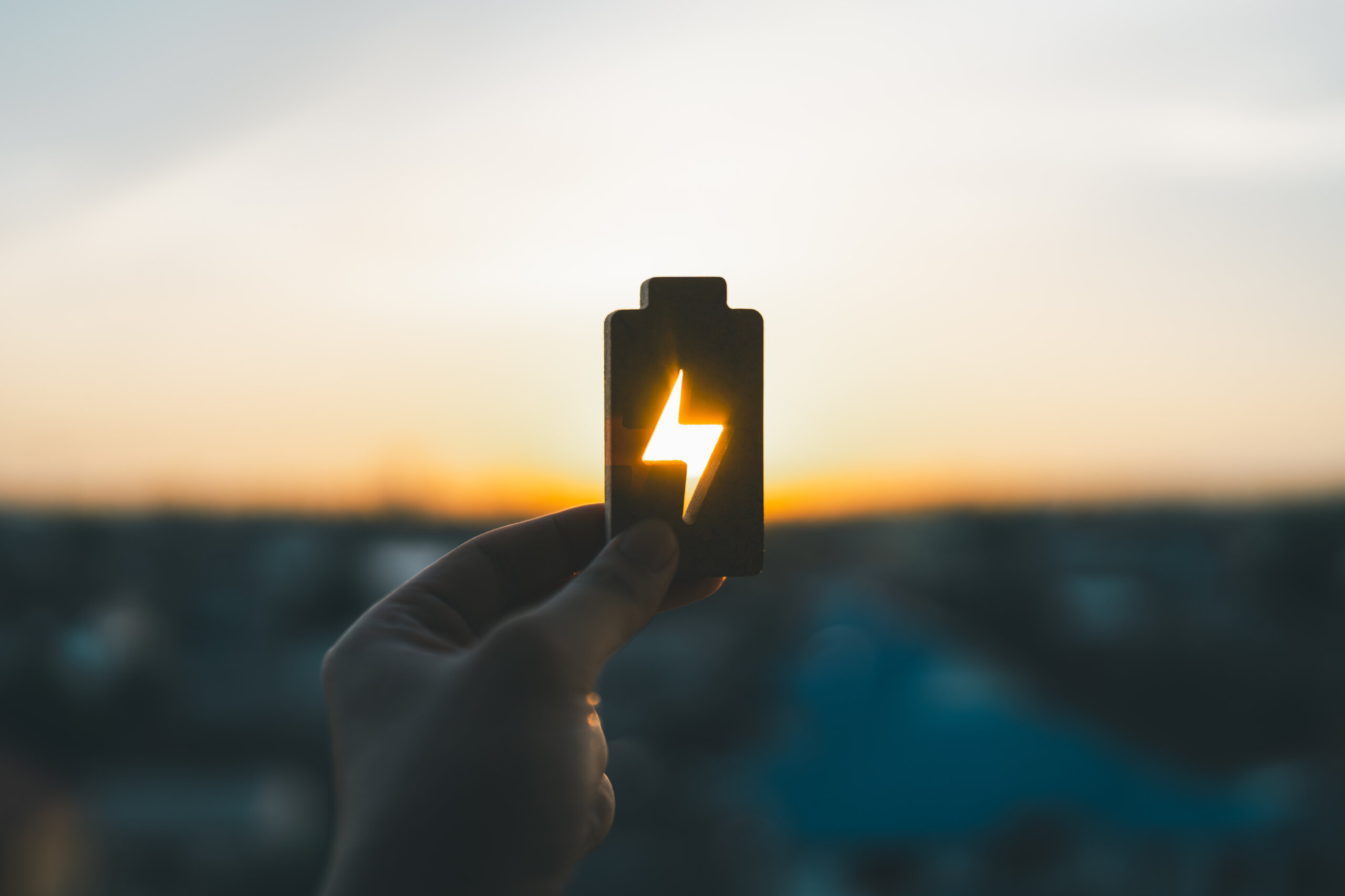A BATTERY BEING HELD UP TO THE SUNSET