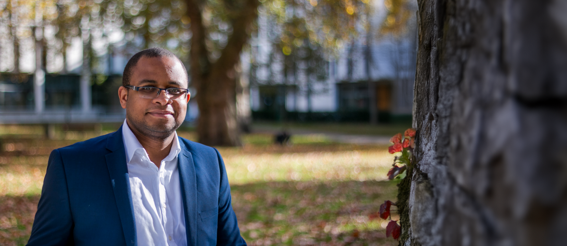 Smartly dressed man starts in green outside green area smiling softly at camera (Freddy Guemeni)