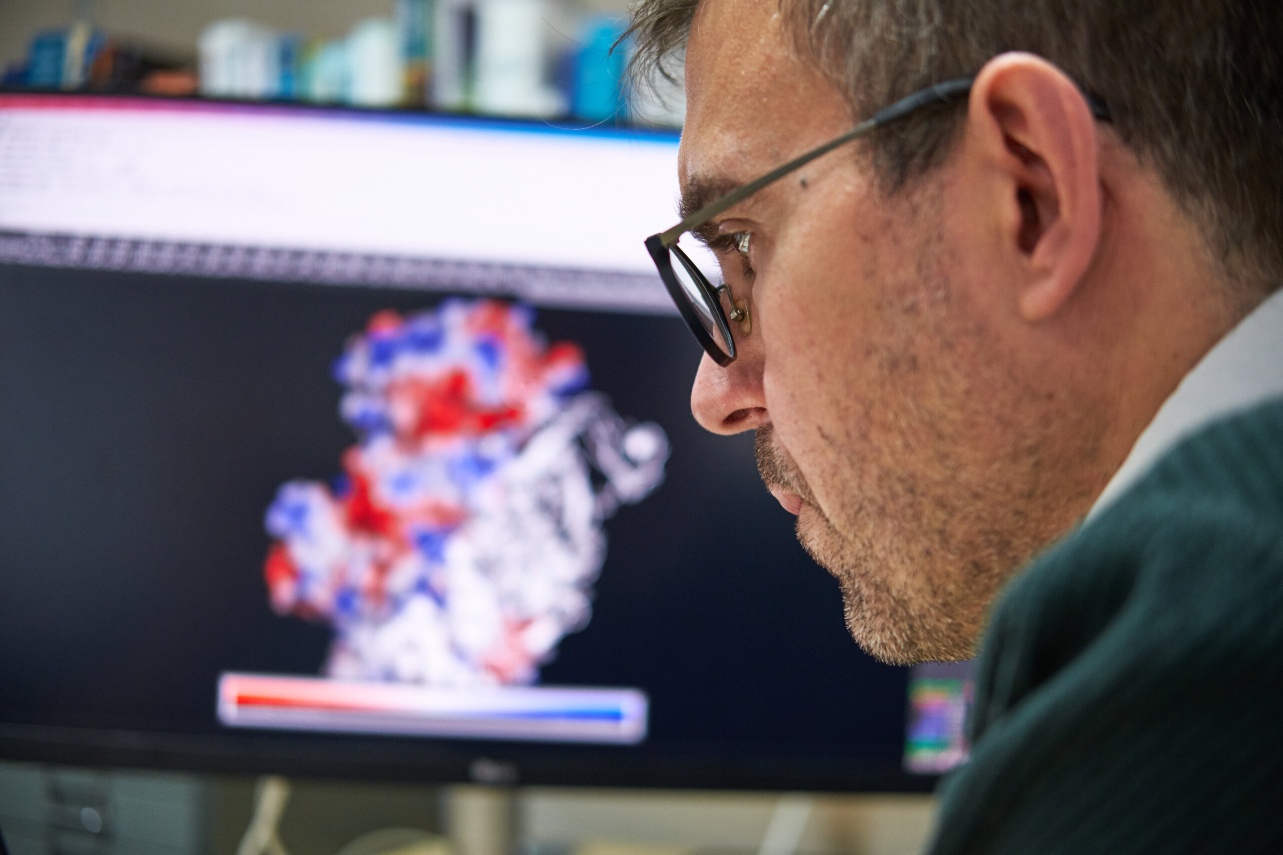 man sits at computer in profile. screen is blurred in background. man wears glasses and is studying something.
