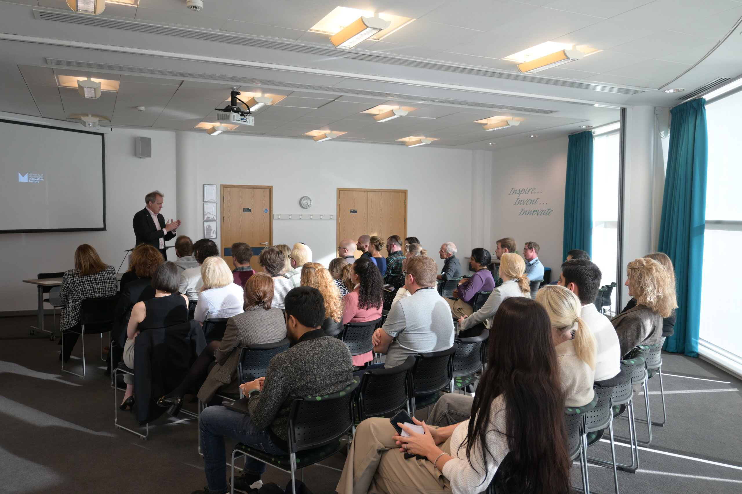 a group of around 30 people sit listening to a presentation