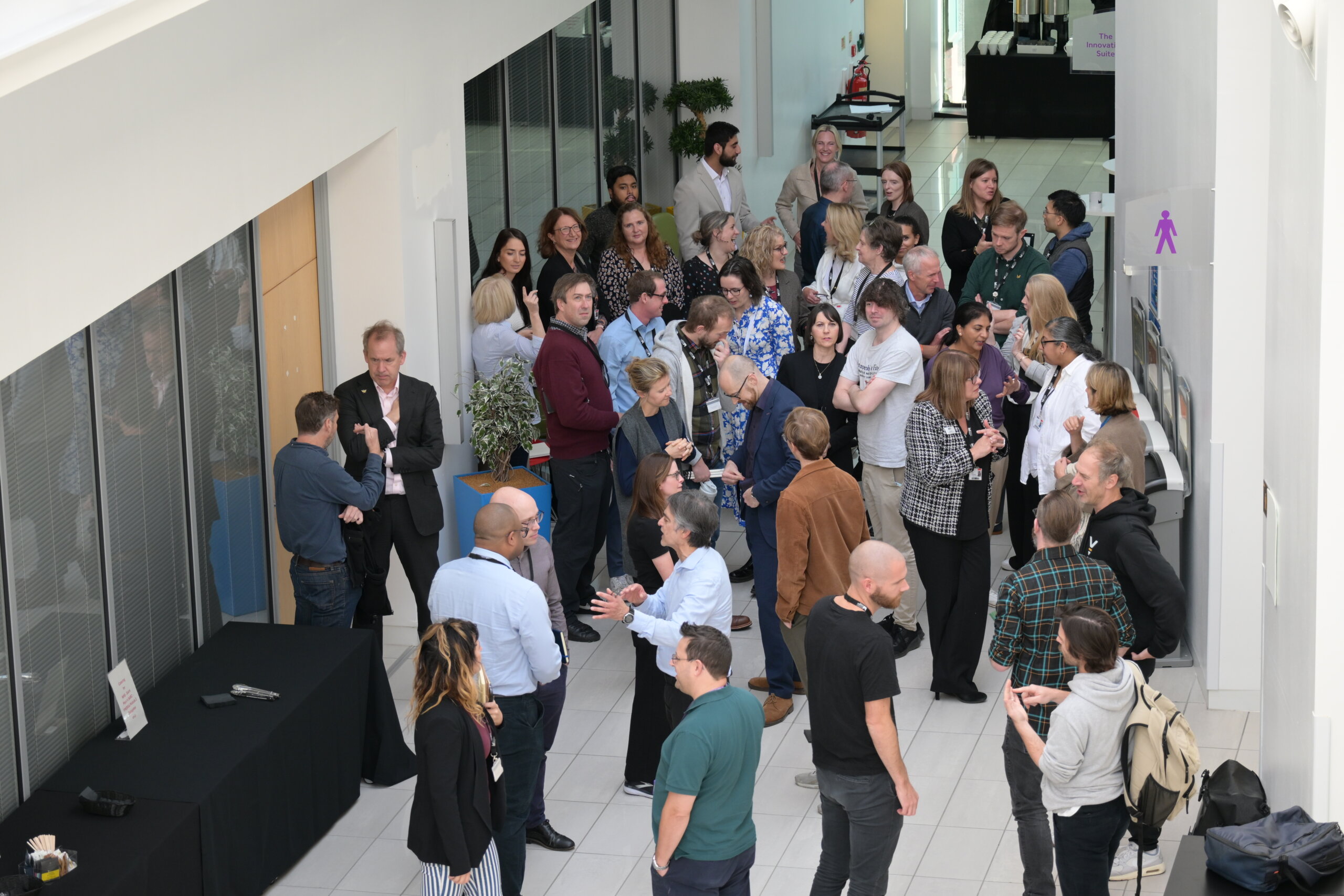 a large group of people stand around chatting in an office communal area