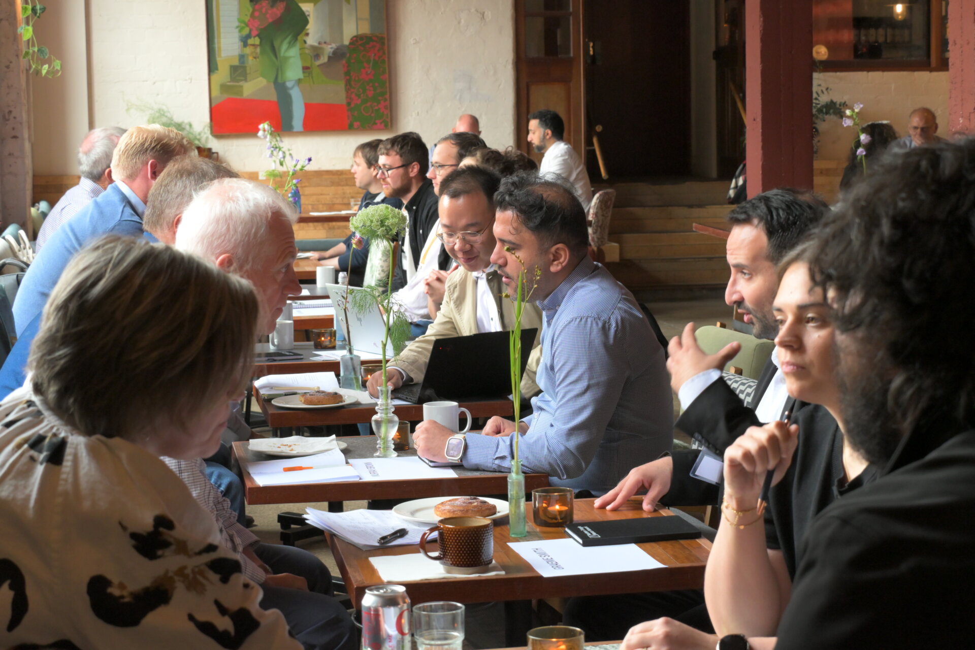 people sit in a row at two person tables in a cafe talking animatedly